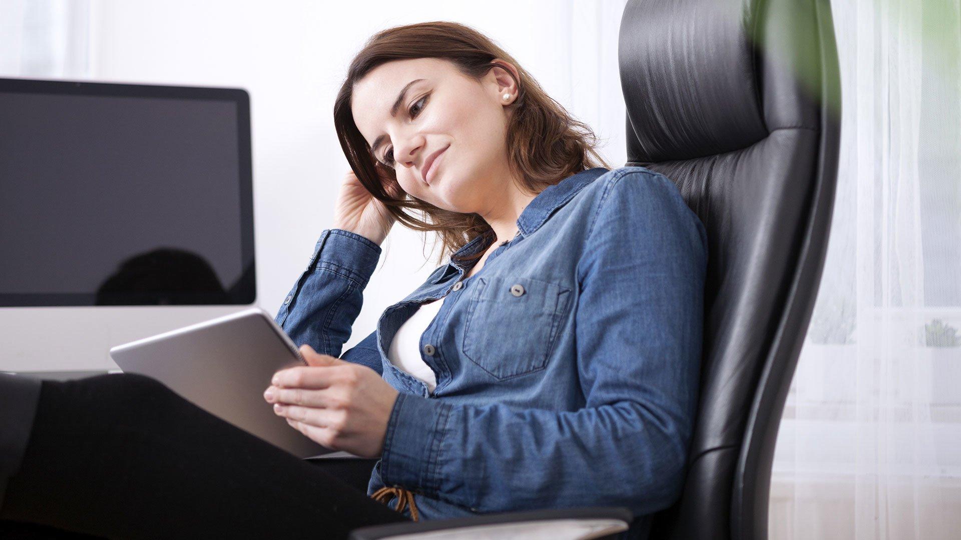 Woman sitting in a black office chair looking at her tablet