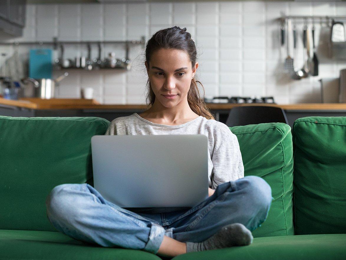 Woman sitting on green sofa while on her laptop