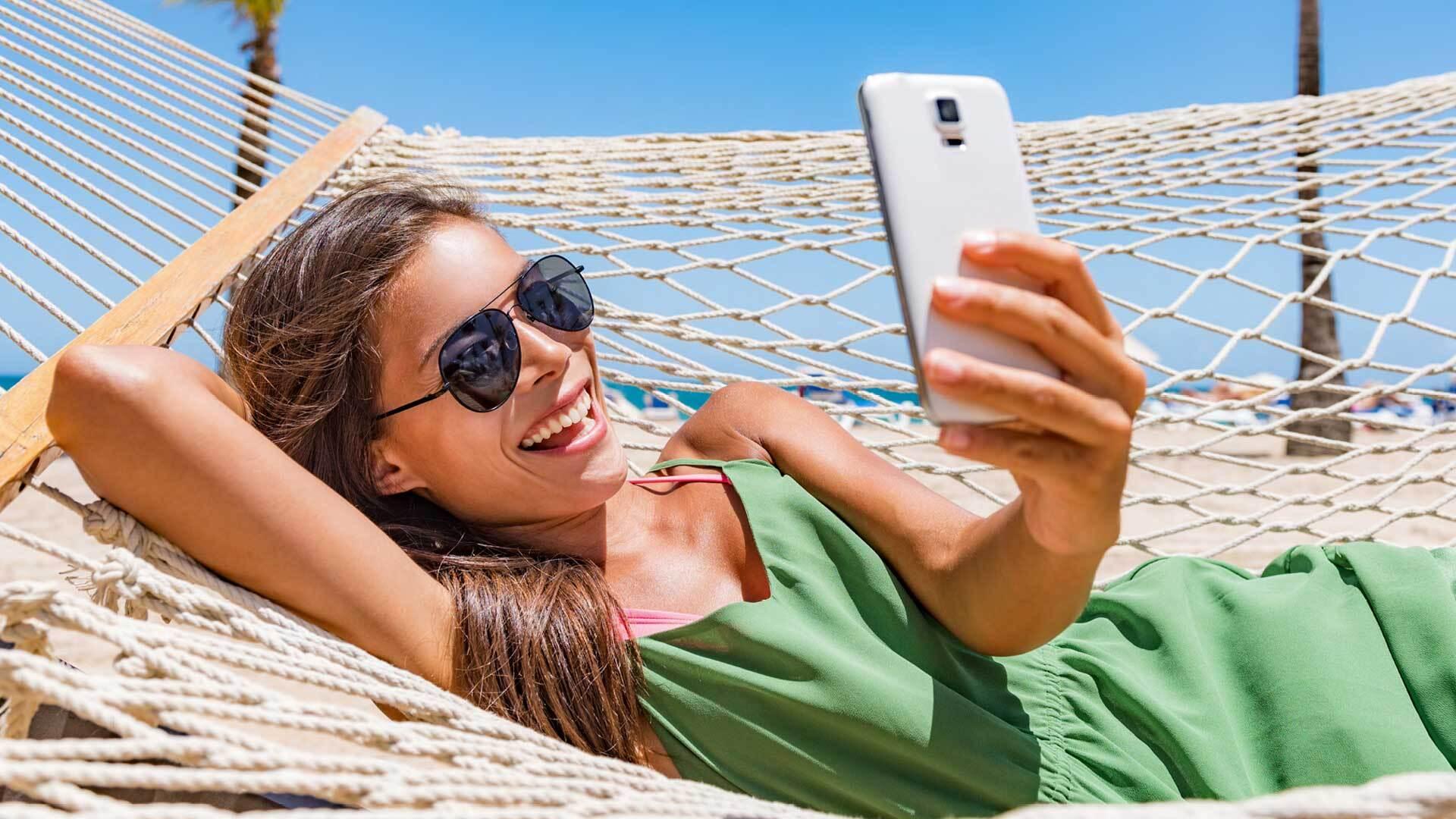 A woman laying in a hammock smiles at her phone