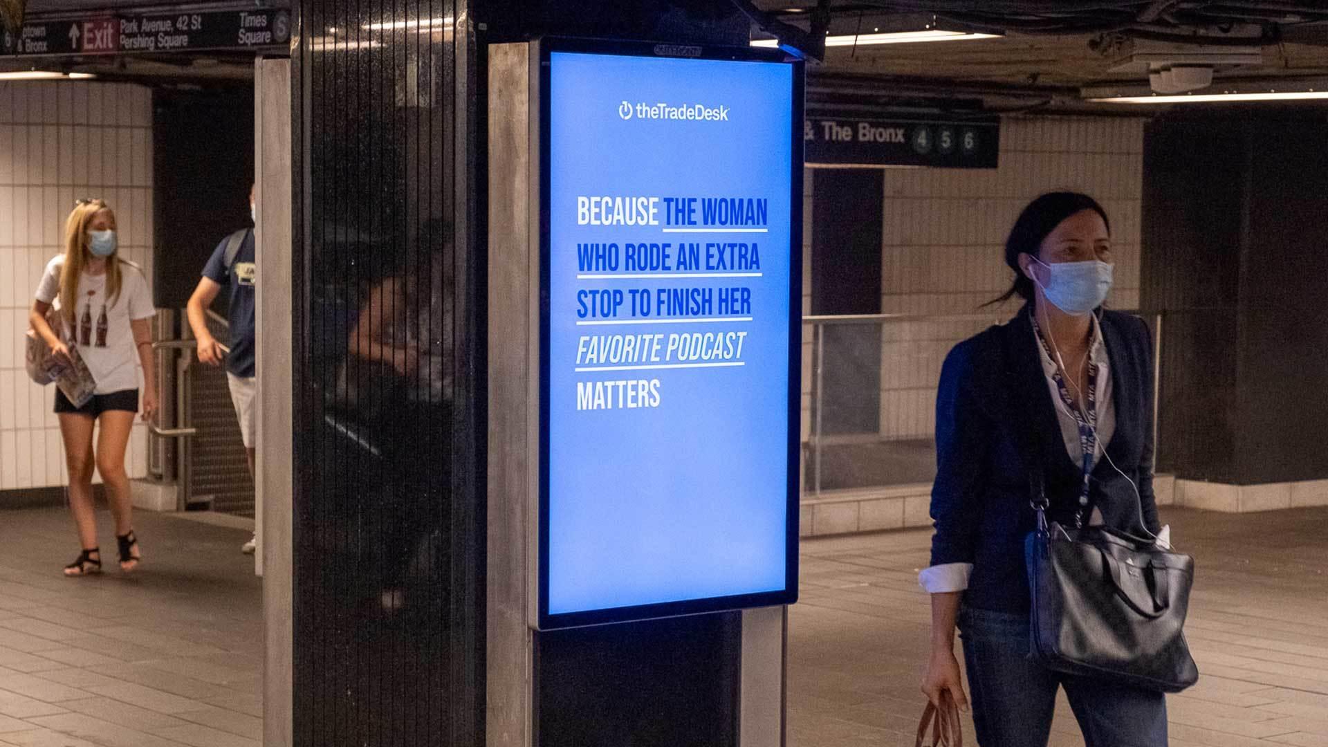 Woman commuter walking past a digital ad for The Trade Desk in a New York subway station